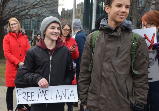 two boys watch protesters at the Womens March, toronto . One of the boys holds a sign that says Free Melania. 