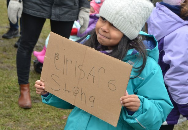 a young girl holds a sign that says girls are strong. She's written it herself on cardboard. 