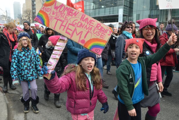 a girl in pink is holding a sign that says WOmen have rights and we're gonna use them. She is shouting as she marches, Womens March, toronto . There are other kids with her 