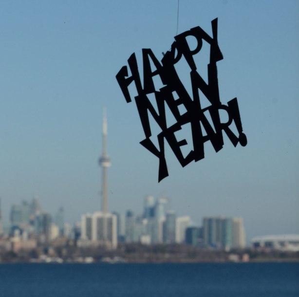a happpy new year sign hangs from the ceiling in a window, the view from the window is in the background, the Toronto skyline with the CN Tower and Lake Ontario