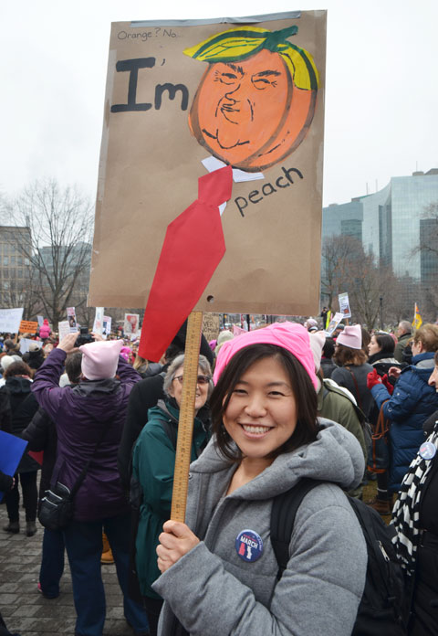 a woman is holding a sign at the Womens March, toronto . Donald Trump's head is shaped like a peach and the words say Im peach. 