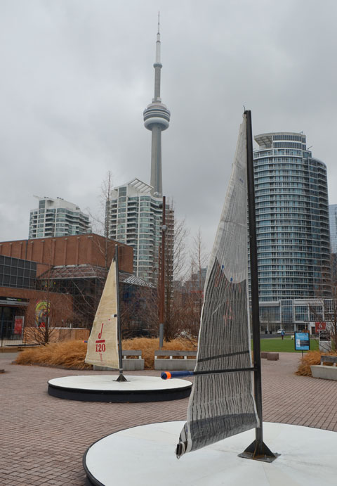 art installation beside Lake Ontario on Toronto's waterfront, called Leeward Fleet, by RAW consulting, two (of three) round platforms with a small sail in the middle. The boom of the sail is the handle for turning the platforms round and round like a merry go round. CN Tower in the background as well as some of the downtown condos. 