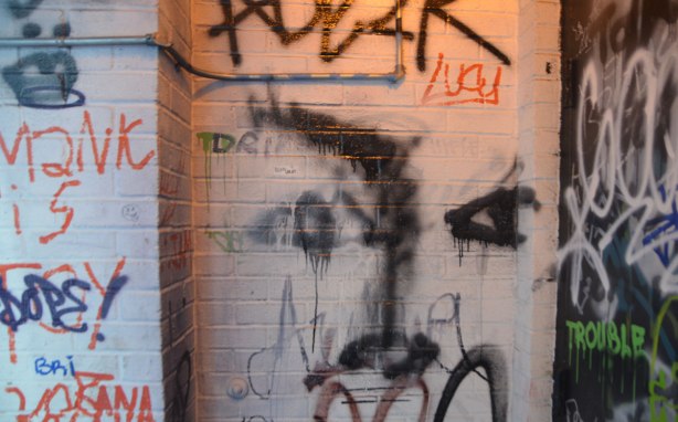 in a dimly lit doorway, a lot of scribbles and graffiti including a roughly drawn face, the word Lucy and the word trouble