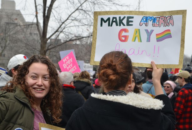 A woman holds up a sign that says Make America Gay again. Lots of other people around her at Queens Park at the start of the Womens March, toronto 