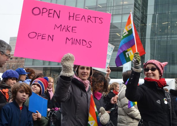 a young woman holds up a large pink sign that says open hearts make open minds. Womens March, toronto 