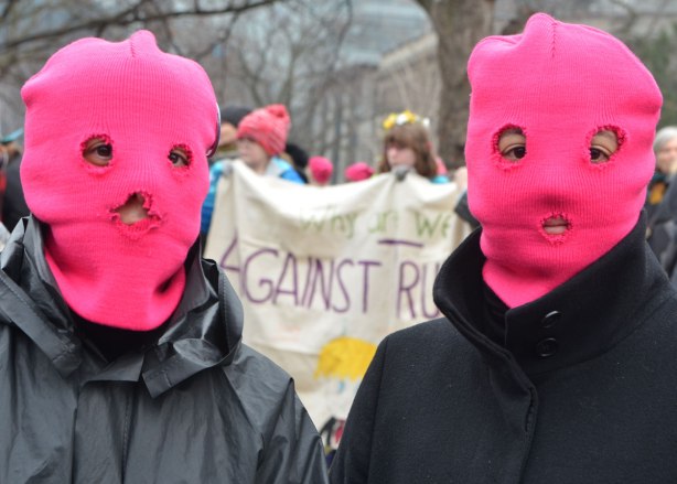 two people wearing pink hats pulled down over their faces with three holes cut in it, two for eyes and one for mouth. At a protest rally against Donald Trump