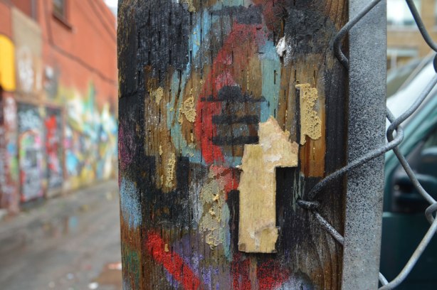 a tiny bit of a stikman is left on a post that is covered with spray paint.