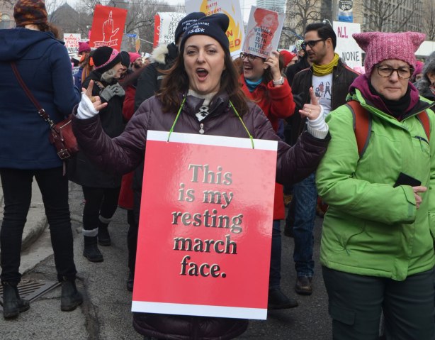 Womens March, Toronto, a woman with a red sign saying This is my resting march face, hams it up for the camera 