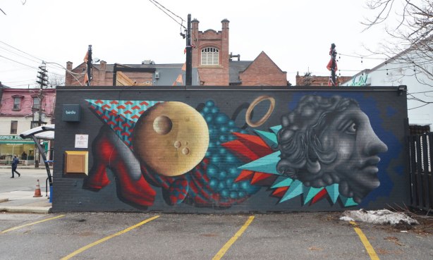 birdo mural on the side of a building, a red high heel shoe, a brown circle, a grey head plus the colourful geometric shapes often found in a birdo mural, in reds and turquoise