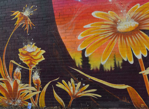 part of a larger mural, yellow daisy like flowers growing on a black background with a large yellow, orange and red circle in the background. 