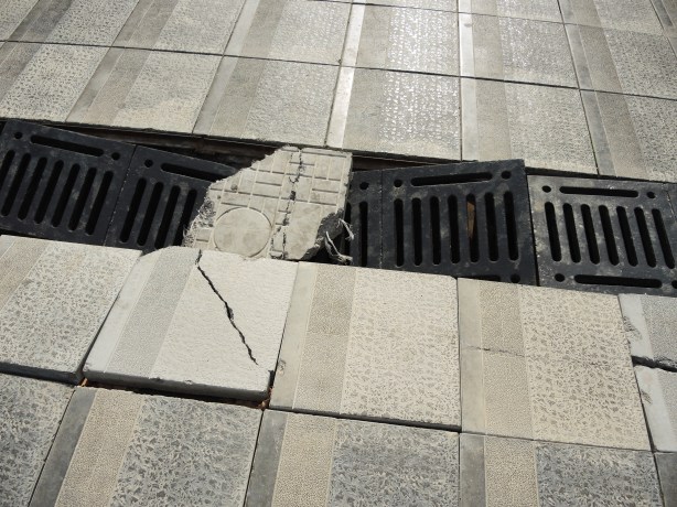 broken tiles on the sidewalk and broken metal drain covers as well