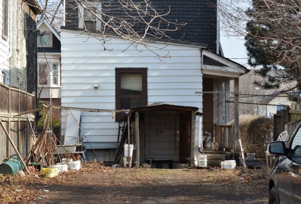 side yard and side entrance to a wood clapboard house with one window on the side at ground level. 