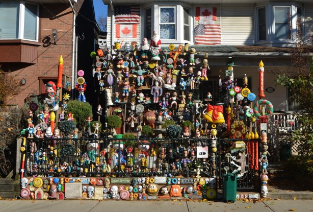 the front yard of a semi detached house is full of toys and stuffed animals, signs and flags, and Christmas decorations, 