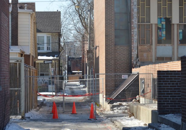 orange cones and a construction fence block entrance to an alley beside a church that is being demolished