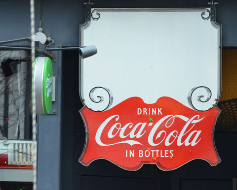 a red and white drink coca cola sign sign hangs in a window of a bar 