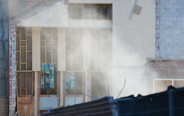 dust from demolition drifts up and past church stained glass windows that are now seen more clearly because one of the exterior walls has been partially removed