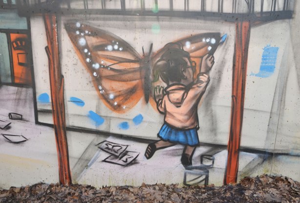 mural by elicser in the tunnel that is a railway underpass - a girl is painting a large picture of a monarch butterfly on a wall 