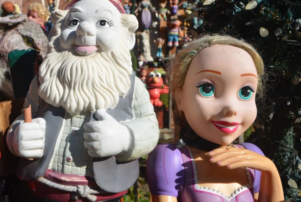 a white plastic gnome and a Disney princess are among a large collection of toys in a front yard 