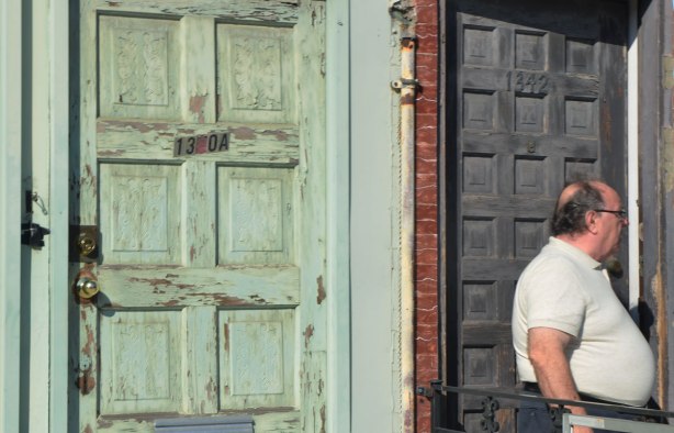 two doors, one faded green and one greyish black . a man with a rather large stomach is standing in front of the latter. 