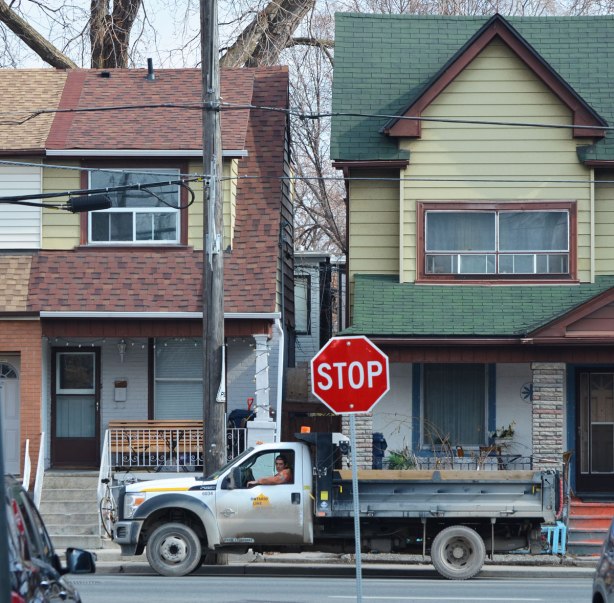 looking down a street to an T-intersection. Two houses across the intersection with a large truck parked in front of them. A man is sitting in the truck and looking at the camera 