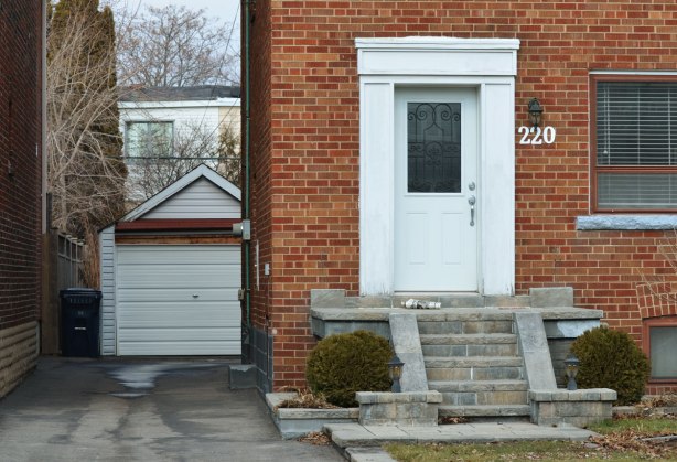 a red brick house with a white rectangular doorway. driveway beside the house leads to a garage with a white door. 