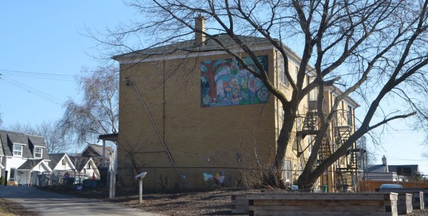 path through a community garden continues past a large house and then towards a street