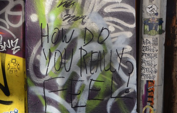graffiti on a wall, a lovebot sticker, a tbonez sticker, and the words How do you really feel?