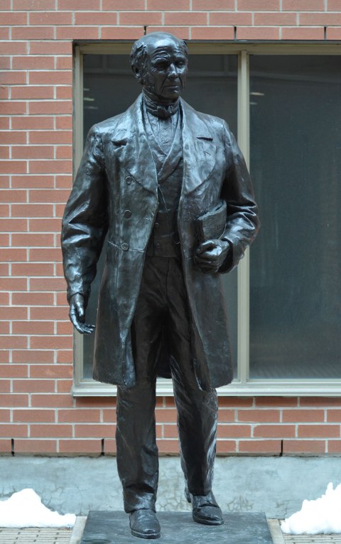 a black bronze statue of James Beaty, standing with a folded newspaper under his arm, about life sized, 