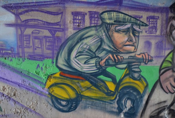 mural by elicser in the tunnel that is a railway underpass - an older man on a motorized scooter, he looks sad, frowning. 