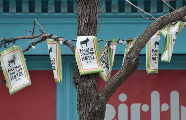 banner made of flags for the Pacific Junction Hotel strung in a tree on the sidewalk 