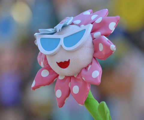 a toy flower with a green stem, petals made of pink fabric with white polka dots, red lips and large white and blue sunglasses. 