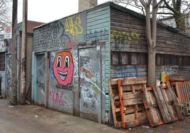 garage in an alley with a big pink and orange face with black and white eyes and big smiling mouth with lots of white teeth 