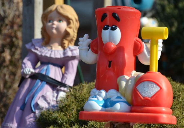 a red plastic toy in the foreground, a doll in a purple dress in the background