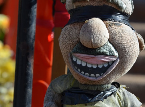 a stuffed plushie creature is attached to a pole with black electrical tape around his face such that it covers his eyes 