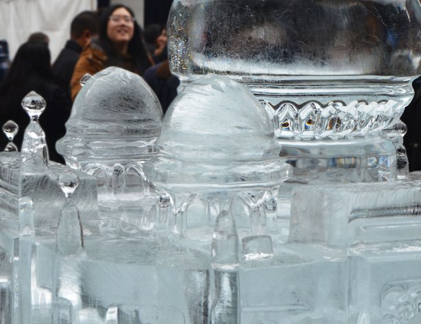 a woman is standing behind an ice sculpture of the taj mahal. 