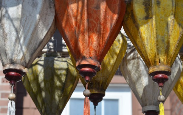 hanging lantern shapes made of fabric, with tassles at the bottoms, hanging over a gate, yellow, green, orange and white