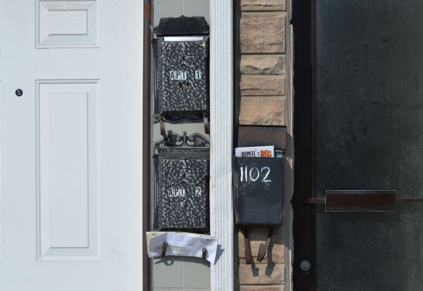 three black mailboxes with mail in them, between a white door and a black door. 