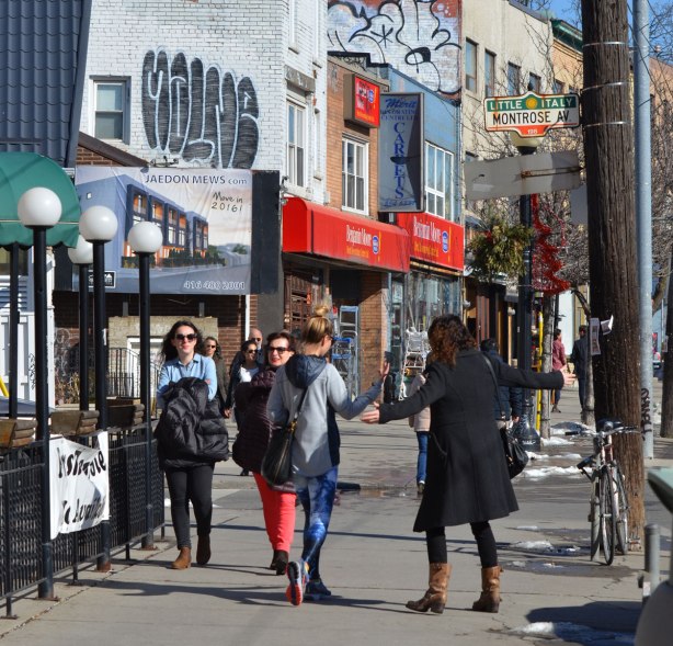 a group of women walking down College Street at Montrose on a sunny winter day. One of the women is wearing a black coat and she has her arms open wide. 