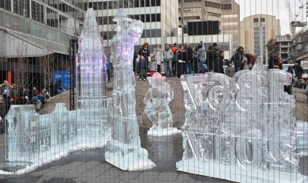 people standing on a large rock to look at ice sculptures of the Parliament buildings in Ottawa, a tall RCMP mountie and the numbers 1867 2017 .