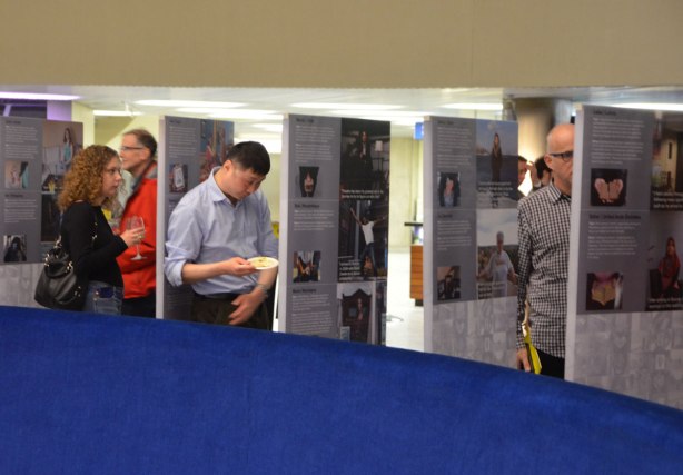 people looking at an exhibit of photos and stories that are printed on upright posters standing on the floor.
