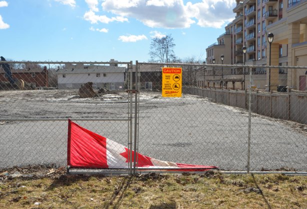 a banner of the Canadian flag has fallen over and is lying on the ground behind a chainlink fence 