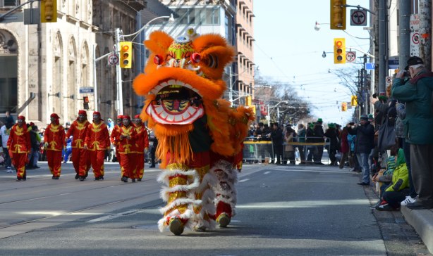 chinese dragon, with two people inside it working it, walking down the street in a parade with spectators standing on the sidewalk