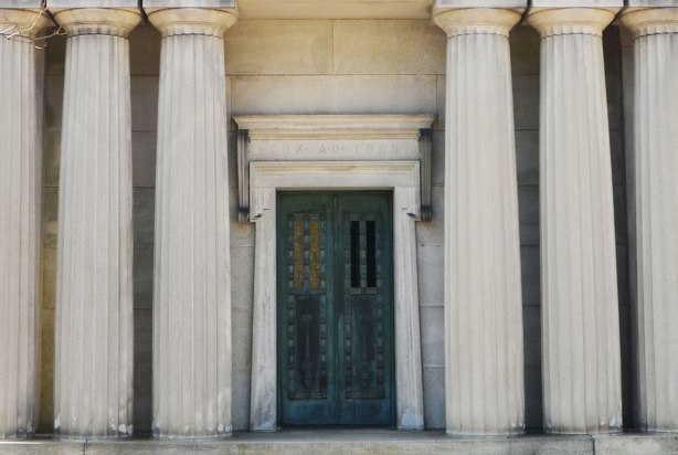 a metal door in a building in a cemetery, three large columns on each side of the door 