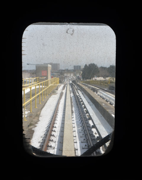 looking out the dirty window at the back of a SRT vehicle, tracks and some cityscape 