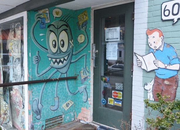 the door of a book store, with a cut out of Tintin beside it and a drawing of a creature with 4 legs and 4 arms, the hands are all holding something 