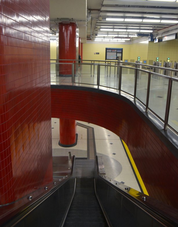 looking down the main escalator at Bessarion subway station, the upper level has yellow walls and the lower level (track level) can also be seen. 