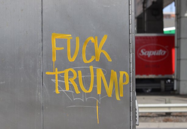 in yellow paint, graffiti, words fuck trump written on a metal box on a sidewalk 