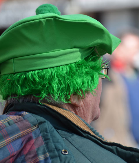 from the back, not much of his face is visible, a man wearing a green wig and a green tam with a pom pom on top