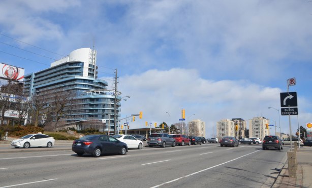 main road with traffic, coming to an intersection, with a tall building in the background 