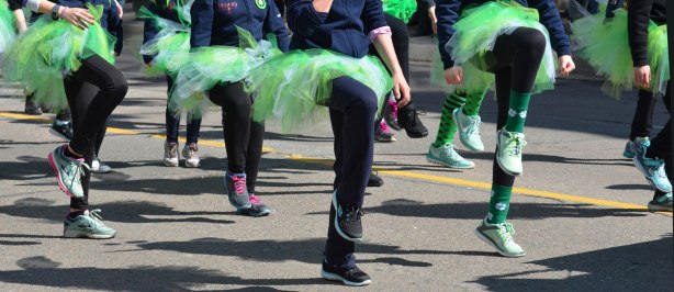 legs and feet of girls in frilly green tutus as they dance in a parade